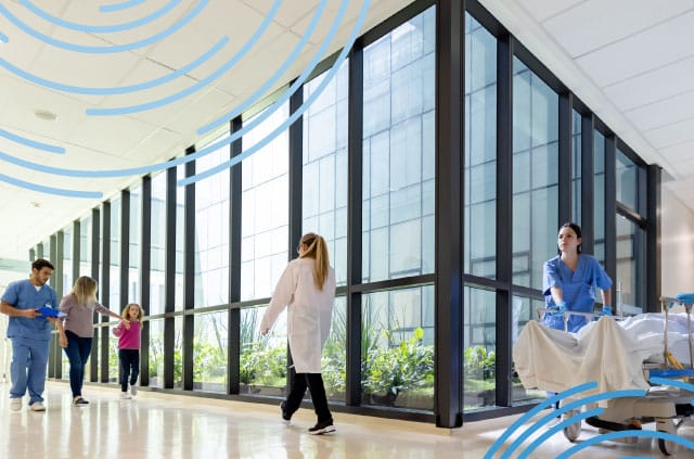 Image of a hospital hallway with a nurse pushing a patient in a bed and people walk by them